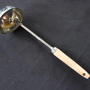 May include: A silver ladle with a wooden handle. The ladle has a rounded bowl and a long, slender handle.