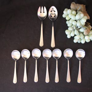 May include: A set of ten silver spoons and two silver serving utensils. The spoons are arranged in a row, with the serving utensils at either end. The serving utensils have a slotted design.