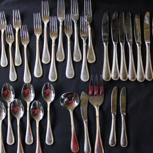 May include: A set of silverware, including forks, knives, and spoons, laid out on a black surface. The silverware is made of polished stainless steel.