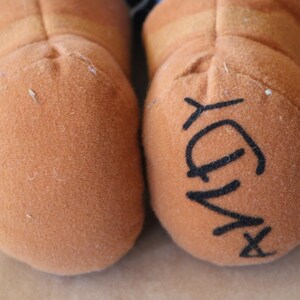 Puede incluir: Primer plano de dos pies de peluche marrones con una firma negra que dice "X-Ray" en un pie.