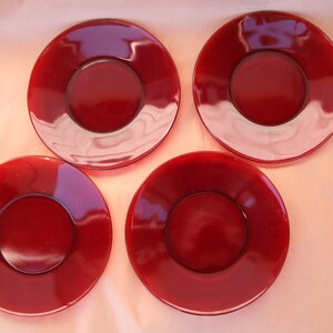 May include: Four red glass plates with a raised rim and a smaller inner circle. The plates are all the same size and shape.