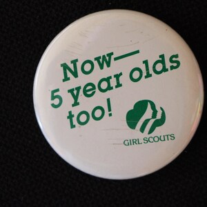 May include: White button with green text that reads "Now - 5 year olds too!" and a green Girl Scout logo.