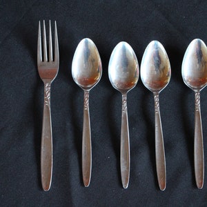 May include: A set of five silver utensils, including a fork and four spoons. The utensils have an ornate design and are arranged in a row on a black surface.