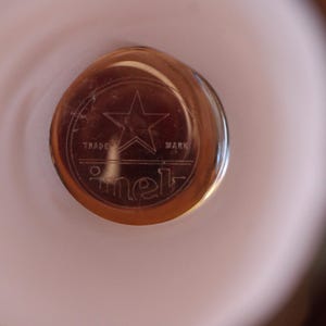 May include: A circular amber-colored glass object featuring an etched design of a five-pointed star centered above the words TRADE MARK and the text imet in a stylized lowercase font, all enclosed within a circular border on a smooth surface.