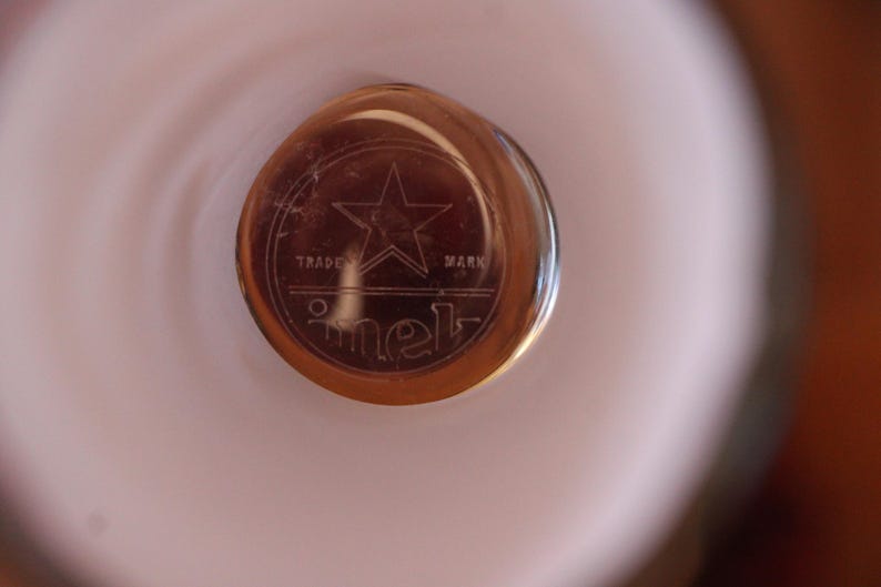 May include: A circular amber-colored glass object featuring an etched design of a five-pointed star centered above the words TRADE MARK and the text imet in a stylized lowercase font, all enclosed within a circular border on a smooth surface.