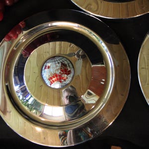 Puede incluir: Juego de tres platos decorativos de metal con una superficie brillante y reflectante. Cada plato presenta c&iacute;rculos conc&eacute;ntricos, con un dise&ntilde;o central de un globo terr&aacute;queo. El dise&ntilde;o del globo tiene detalles en rojo y blanco.