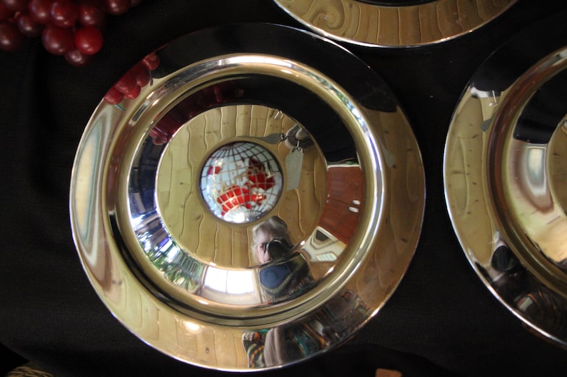Puede incluir: Juego de tres platos decorativos de metal con una superficie brillante y reflectante. Cada plato presenta c&iacute;rculos conc&eacute;ntricos, con un dise&ntilde;o central de un globo terr&aacute;queo. El dise&ntilde;o del globo tiene detalles en rojo y blanco.
