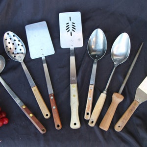 May include: A set of eight kitchen utensils with wooden handles. The utensils include a ladle, a slotted spoon, a spatula, a slotted turner, two spoons, a knife sharpener, and a spatula.