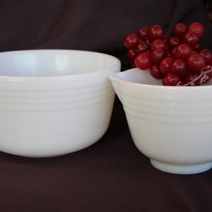 May include: Two white mixing bowls, one larger than the other, with a cluster of red grapes in the smaller bowl.
