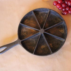 May include: A cast iron pan with a black handle and seven sections. The pan is designed for making individual portions of food.