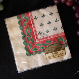 May include: A package of Hallmark luncheon napkins. The napkins are square, with a cream-colored background and a red and green holly border. The napkins are packaged in clear plastic. The package also has a label that reads "16 Napkins".