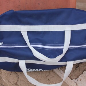 May include: A blue duffel bag with white straps and a zipper. The bag has the word "TOMMY" printed on the bottom.