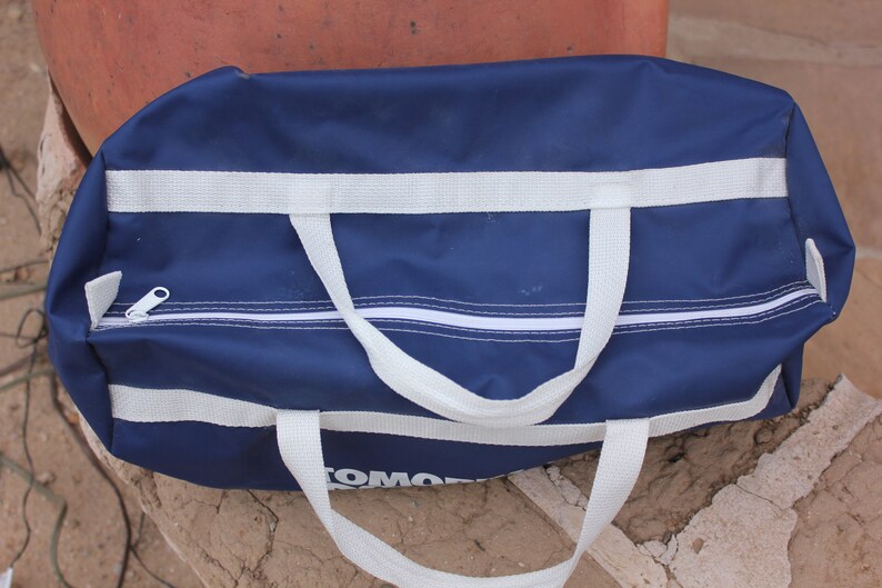 May include: A blue duffel bag with white straps and a zipper. The bag has the word "TOMMY" printed on the bottom.