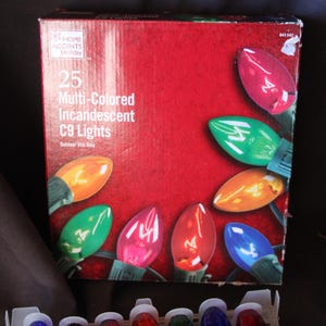May include: A rectangular box of 25 multi-colored incandescent C9 lights by Home Accents Holiday. The red packaging features images of pink, green, orange, and blue light bulbs. The text reads 25 Multi-Colored Incandescent C9 Lights.