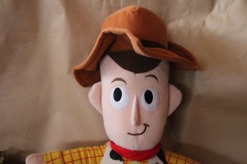 Puede incluir: Un juguete de peluche de Woody de la franquicia Toy Story. Lleva un sombrero de vaquero marr&oacute;n y una camisa de cuadros amarillos y rojos. Tiene una expresi&oacute;n amigable en su rostro.