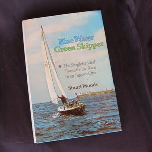 May include: A book titled "Blue Water Green Skipper: The Singlehanded Transatlantic Race from Square One" by Stuart Woods. The cover features a sailboat on the water.