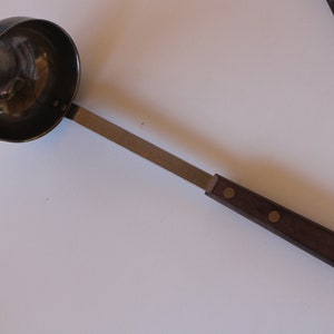 May include: A silver ladle with a brown wooden handle. The handle has two brass accents.
