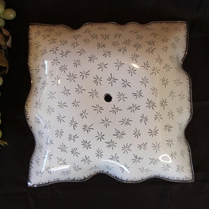May include: A white glass ceiling light fixture with a scalloped edge and a starburst pattern. The fixture has a single hole in the center for mounting.