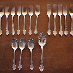 May include: A set of silverware, including forks and spoons, laid out on a wooden table. The silverware is made of polished metal and has an ornate design.