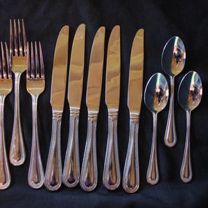 May include: A set of silverware with a beaded design on the handles. The set includes five forks, five knives, and four spoons.