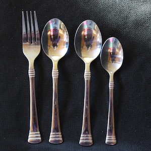 May include: A set of four silver-toned flatware pieces, including a fork and three spoons. The spoons are different sizes, with the largest spoon being the most prominent.