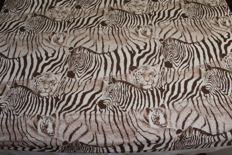 Puede incluir: Una tela con un patr&oacute;n repetitivo de cebras y tigres en marr&oacute;n y blanco. El dise&ntilde;o muestra m&uacute;ltiples cebras en varias posiciones junto a caras de tigres, todo ello en una combinaci&oacute;n de colores marr&oacute;n y blanco consistente.