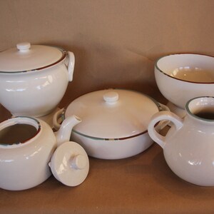May include: A set of five white ceramic kitchenware pieces with brown and green trim. The set includes a teapot, a creamer, a covered casserole dish, a covered soup tureen, and a bowl.