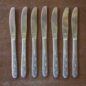 May include: Seven silver dinner knives with a starburst pattern on the handles.