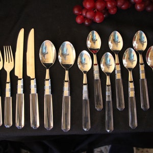 May include: A set of silver cutlery with clear acrylic handles. The set includes forks, knives, and spoons.