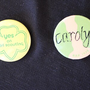 May include: Two round pins with green and yellow designs. One pin says "yes on girl scouting" and the other says "Carolyn RAP 1976".