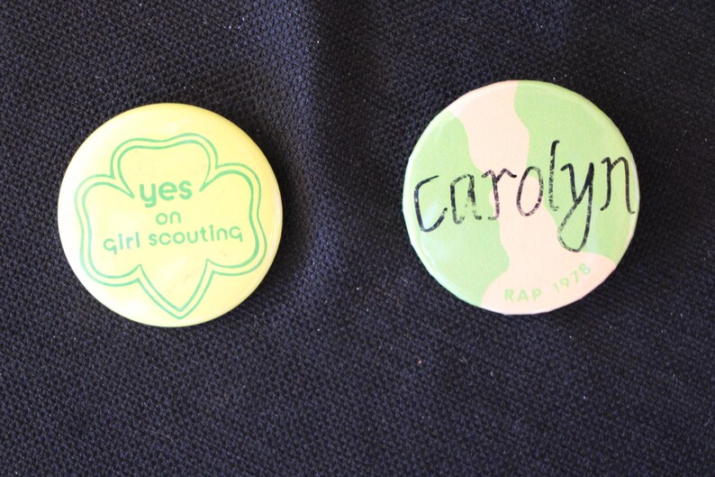 May include: Two round pins with green and yellow designs. One pin says "yes on girl scouting" and the other says "Carolyn RAP 1976".