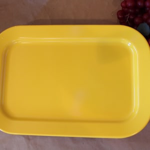 May include: A bright yellow rectangular serving tray with rounded edges. The tray is made of plastic and has a smooth surface.