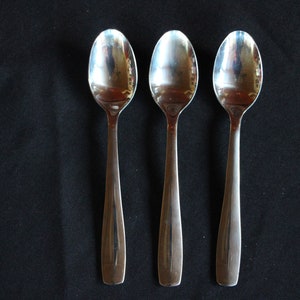 May include: Three silver spoons of varying sizes, arranged in a row on a black surface.