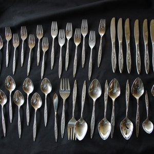 May include: A set of silverware, including forks, spoons, and knives, all with a silver finish and ornate designs. The silverware is arranged in rows on a black surface.