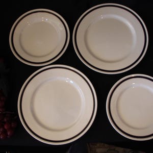 May include: Four white ceramic plates with a black rim. The plates are arranged in a circle on a black surface.