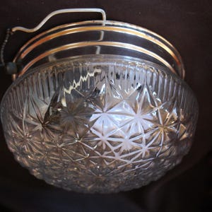 May include: A flush mount ceiling light fixture featuring a clear, dome-shaped glass shade with a pressed starburst and geometric pattern. The fixture includes a metallic gold-toned circular base and exposed black and white electrical wiring.