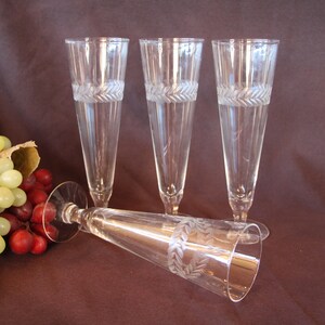 May include: Set of four clear glass champagne flutes with an etched leaf design around the middle of each glass. The glasses are arranged in a group with one lying on its side.