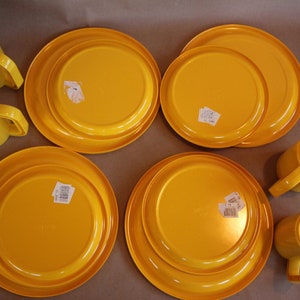 Op de afbeelding: Set van vier gele plastic bekers en vier gele plastic borden. De bekers en borden hebben een eenvoudig ontwerp en zijn perfect voor informele diners.