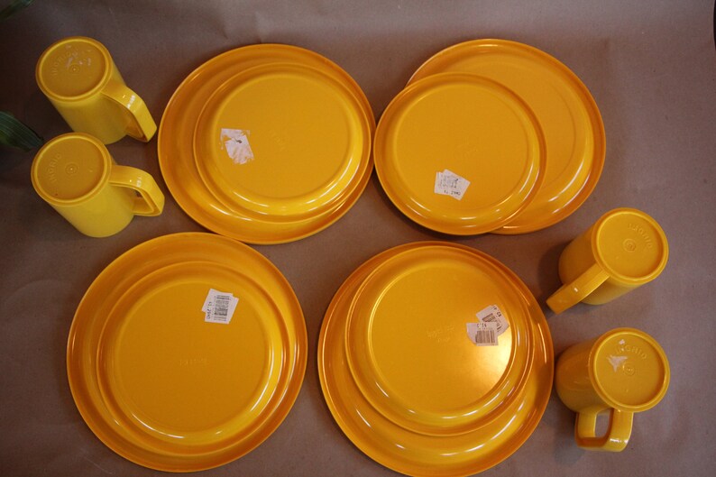 Op de afbeelding: Set van vier gele plastic bekers en vier gele plastic borden. De bekers en borden hebben een eenvoudig ontwerp en zijn perfect voor informele diners.