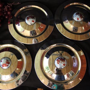 Puede incluir: Cuatro platos de metal vintage con una superficie brillante y reflectante. Cada plato presenta un dise&ntilde;o de globo central con continentes rojos y blancos. Los platos tienen un centro negro y un borde dorado.