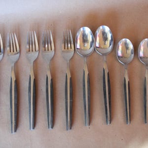 May include: A set of eight silver-toned flatware pieces, including forks and spoons. The handles are black and have a wood-like texture.