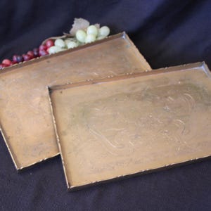 May include: Two gold-colored metal trays with decorative etched designs. The top tray is plain, while the bottom tray has a more intricate design.