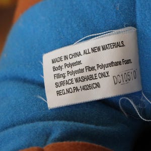 Puede incluir: Etiqueta blanca con texto negro sobre un fondo de tela azul. La etiqueta dice "MADE IN CHINA. ALL NEW MATERIALS. Body: Polyester. Filling: Polyester Fiber, Polyurethane Foam. SURFACE WASHABLE ONLY. REG.NO.PA-14026(CN) DC10510"