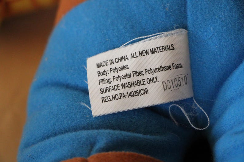 Puede incluir: Etiqueta blanca con texto negro sobre un fondo de tela azul. La etiqueta dice "MADE IN CHINA. ALL NEW MATERIALS. Body: Polyester. Filling: Polyester Fiber, Polyurethane Foam. SURFACE WASHABLE ONLY. REG.NO.PA-14026(CN) DC10510"