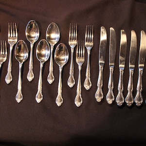 May include: A set of silverware with a silver finish, including forks, spoons, and knives. The silverware has an ornate design with a floral pattern.