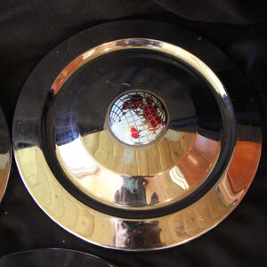 Puede incluir: Un juego de tres platos redondos met&aacute;licos con un centro negro y un borde dorado. Cada plato presenta un dise&ntilde;o de globo en el centro, con continentes rojos y blancos. Los platos son reflectantes y parecen ser de metal.