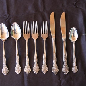 May include: A set of silverware with ornate handles, including two spoons, four forks, and two butter knives. The silverware is arranged on a black surface.