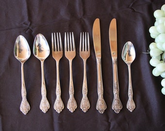 May include: A set of silverware with ornate handles, including two spoons, four forks, and two butter knives. The silverware is arranged on a black surface.