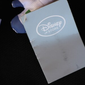 May include: A blue and white tag with the text "Disney Store" in a white circle.