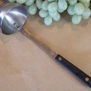 May include: A silver ladle with a black handle. The ladle has a rounded bowl and a long, thin handle.